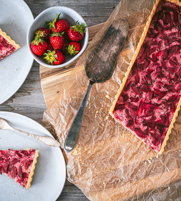 Flatlay einer Rhabarber-Erdbeer-Tarte mit zwei Stücken Tarte auf Tellern