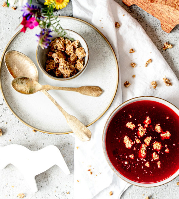 Erdbeersuppe mit Granola, Löffeln Tellern, einem Dalapferd aus Kork und Wiesenblumen